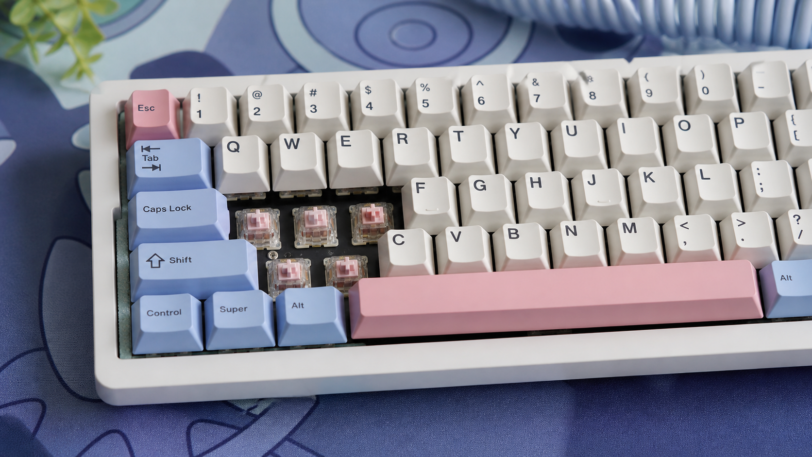 A modded mechanical keyboard with pastel pink and blue PBT keycaps, some keycaps removed to show pink switches underneath
