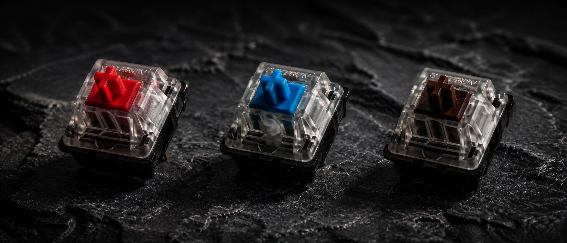 Three mechanical keyboard switches side by side — Cherry MX Red, Blue, and Brown — on a dark surface with dramatic lighting highlighting their colored stems